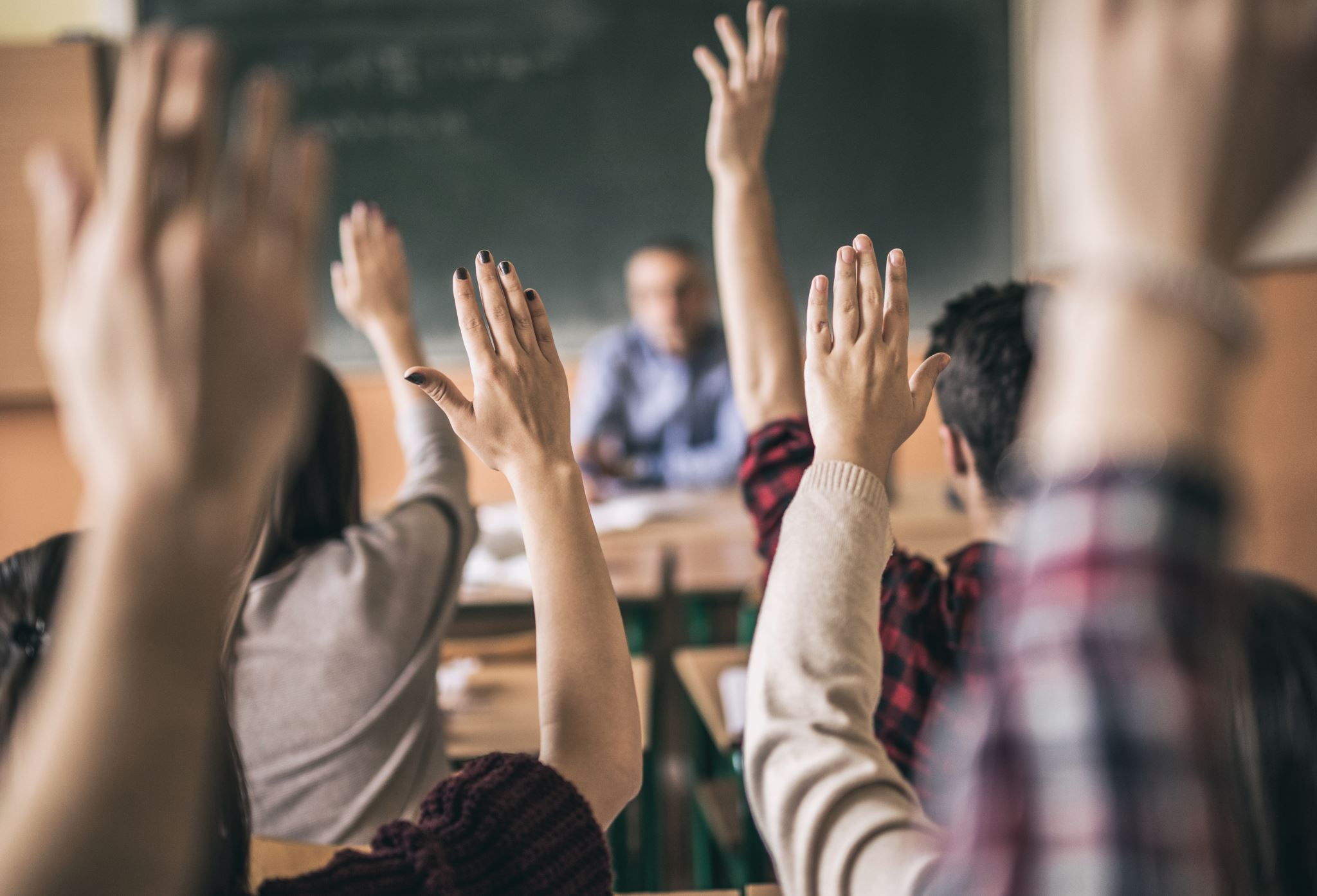 Aufzeigende-Schulkinder-im-Klassenzimmer-vor-Lehrkraft