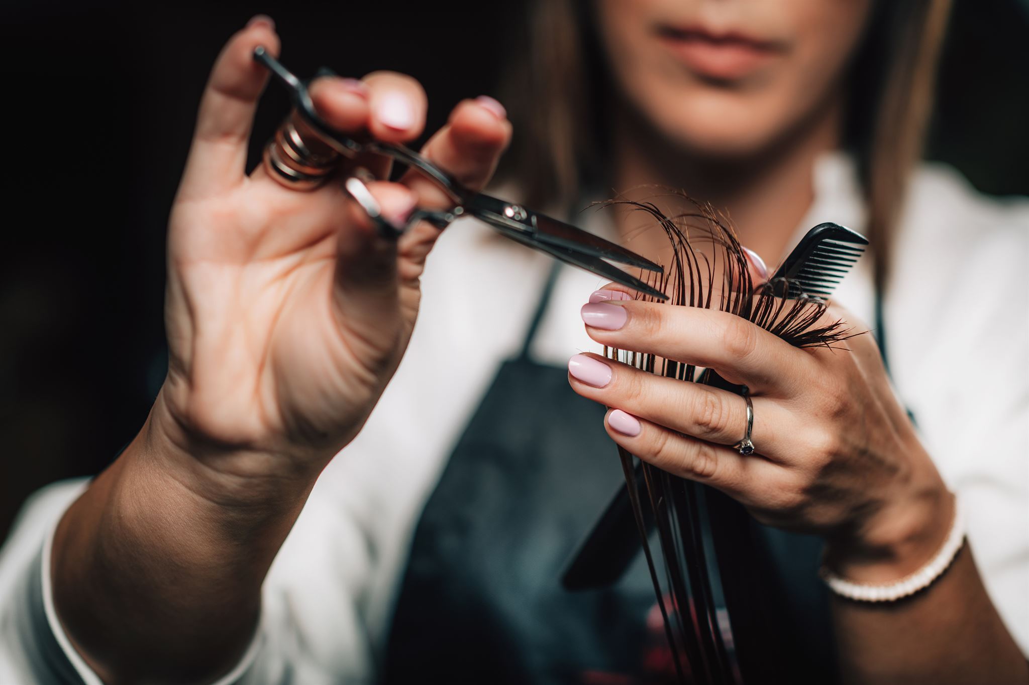 Friseur,-der-mit-einer-Haarschneideschere-die-Enden-der-langen-Haarsträhne-abschneidet,-die-mit-der-anderen-Hand-hochgehalten-wird